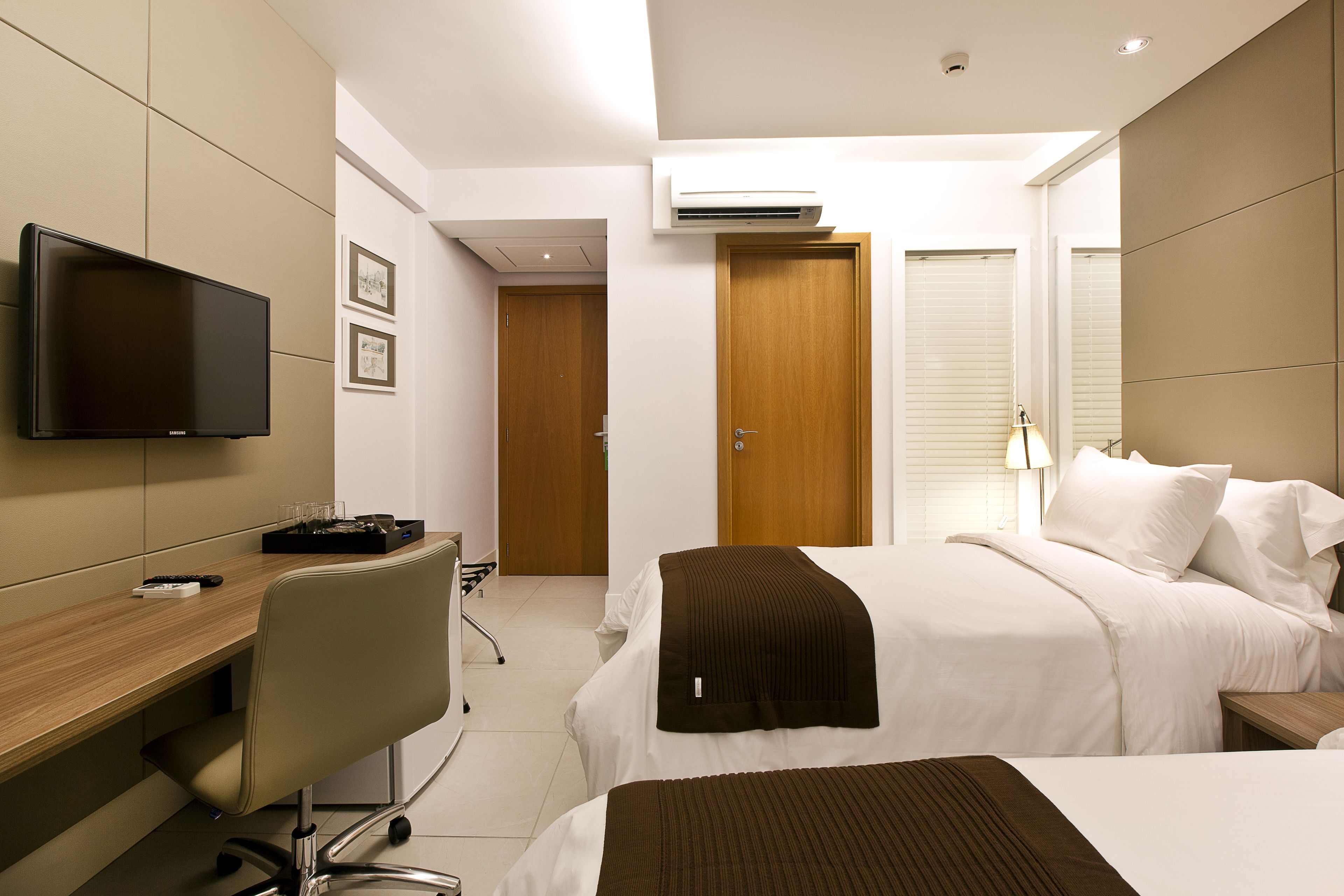 Une chambre d’hôtel moderne équipée d’une télévision à écran plat, d’un bureau avec une chaise, d’un lit avec du linge de lit blanc et d’une porte en bois.
