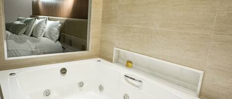 A modern bathroom with a large bathtub, a mirror, and beige tiled walls.
