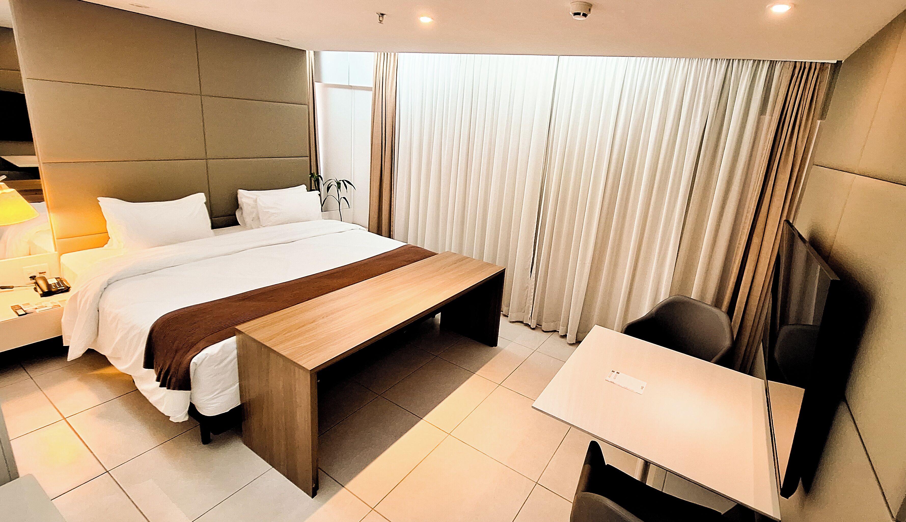 Une chambre d’hôtel moderne avec un grand lit, une table de chevet et un bureau avec une chaise.