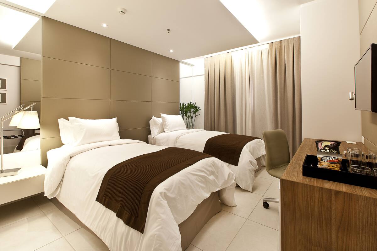 Hotelkamer met twee bedden, een bureau met een dienblad snacks, een lamp en een grote spiegel.