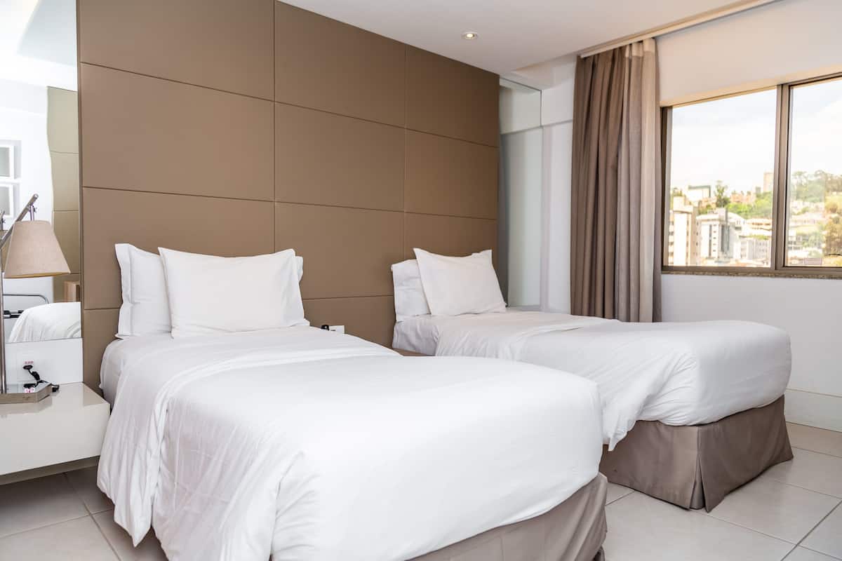 Een hotelkamer met twee bedden, een groot raam met uitzicht op gebouwen en een modern design.
