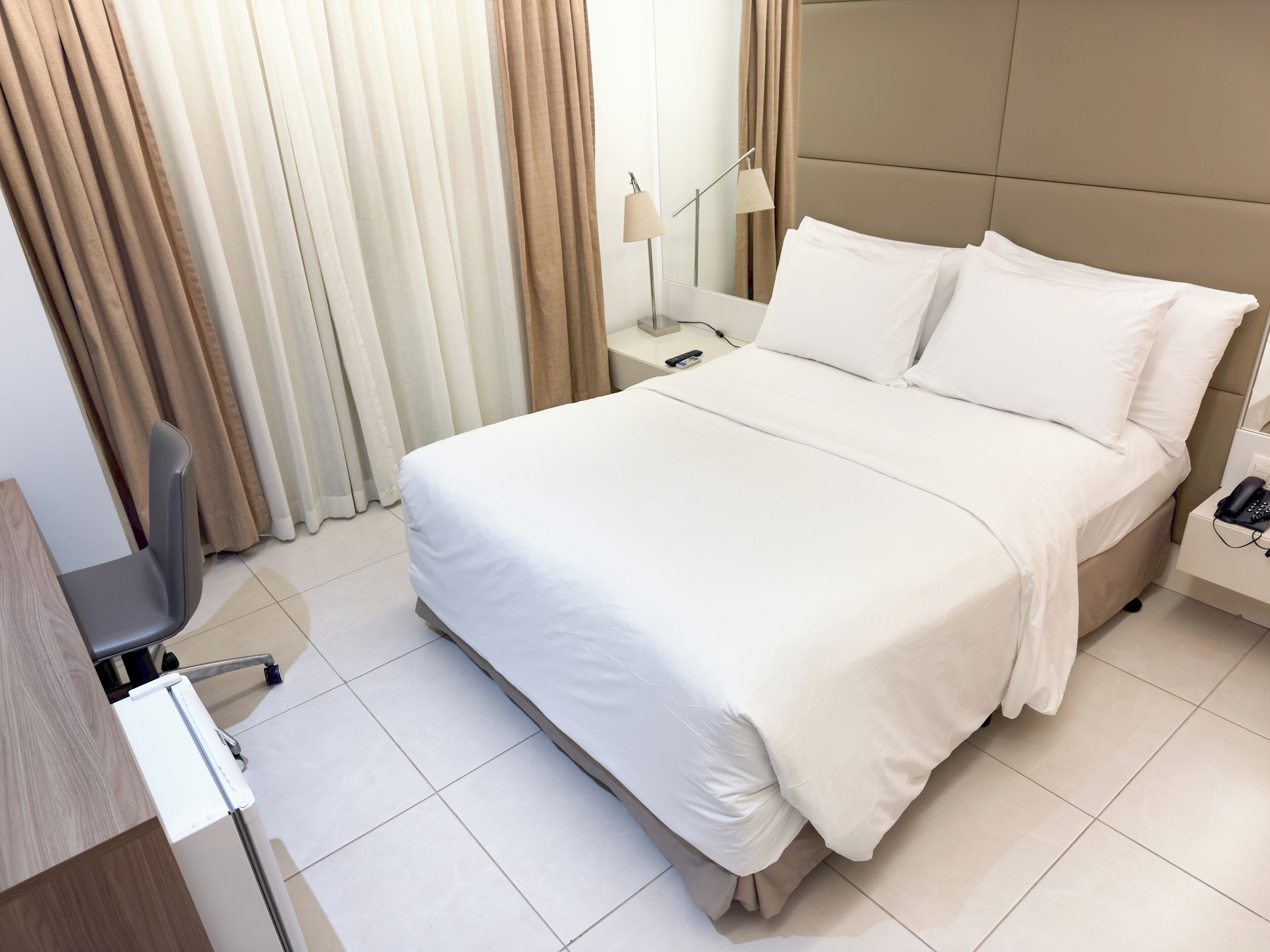 A neatly made bed with white linens, a bedside table with a lamp, and a chair.