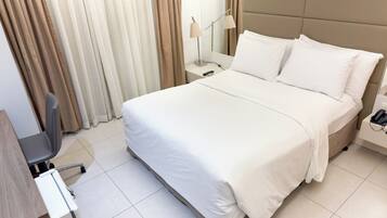 A neatly made bed with white linens, a bedside table with a lamp, and a chair.