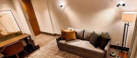 A modern hotel room with a sofa, a desk, and a lamp.