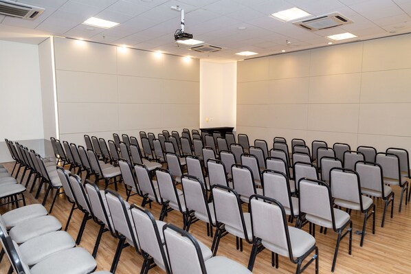 A conference room with rows of chairs, a podium, and a projector on the ceiling.