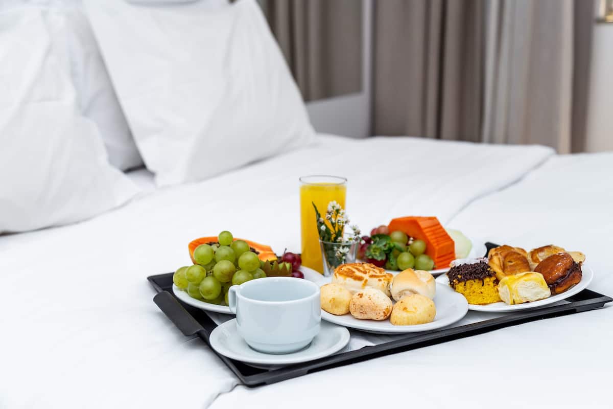 Een ontbijtkarretje met fruit, gebak en een glas sinaasappelsap op een hotelbed.