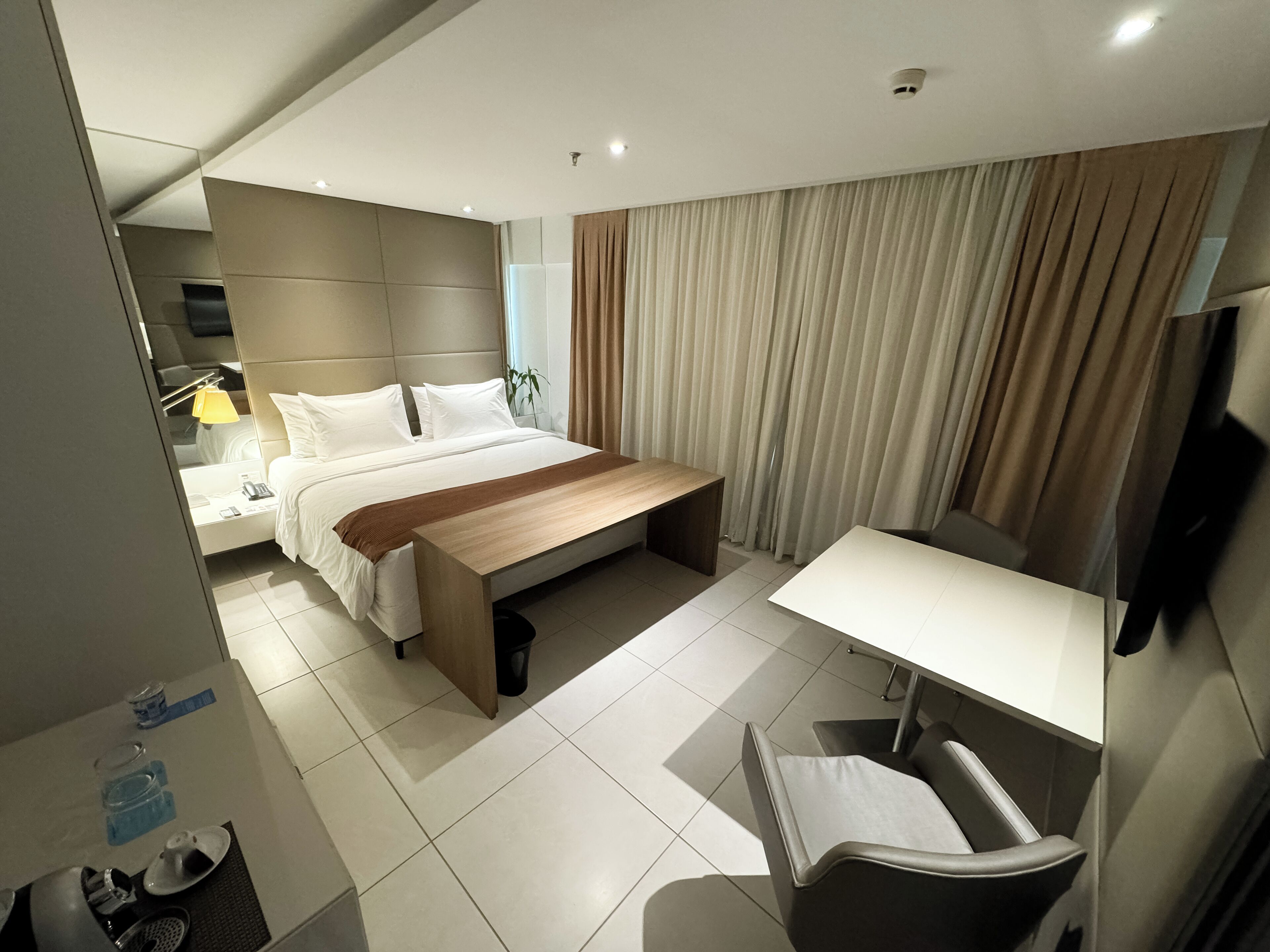 Quarto de hotel moderno com uma cama grande, mesa de cabeceira e escrivaninha com cadeira.