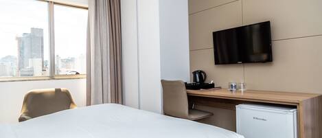 A hotel room with a bed, a desk with a computer, a television, and a refrigerator.