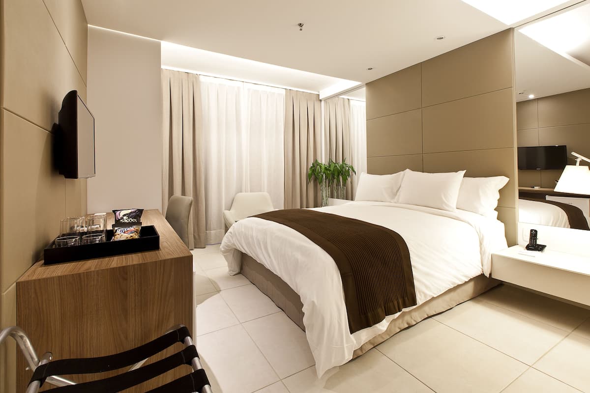Een moderne hotelkamer met een bed, nachtkastje, stoel en een aan de muur bevestigde televisie.