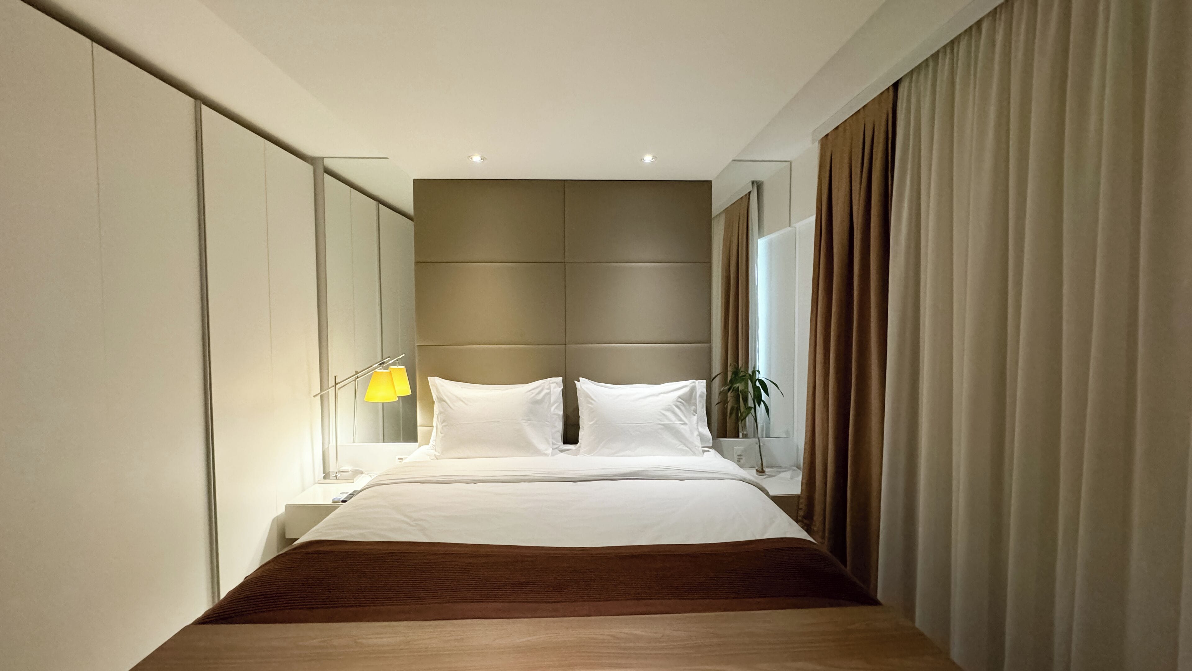 Une chambre d’hôtel moderne avec un grand lit, une table de chevet, une lampe et un miroir.