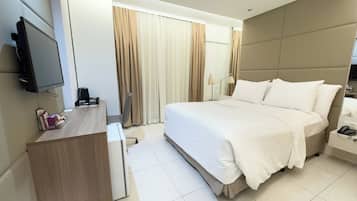 Quarto de hotel moderno com uma cama grande, uma escrivaninha, uma TV de tela plana e uma mesa de cabeceira com abajur.