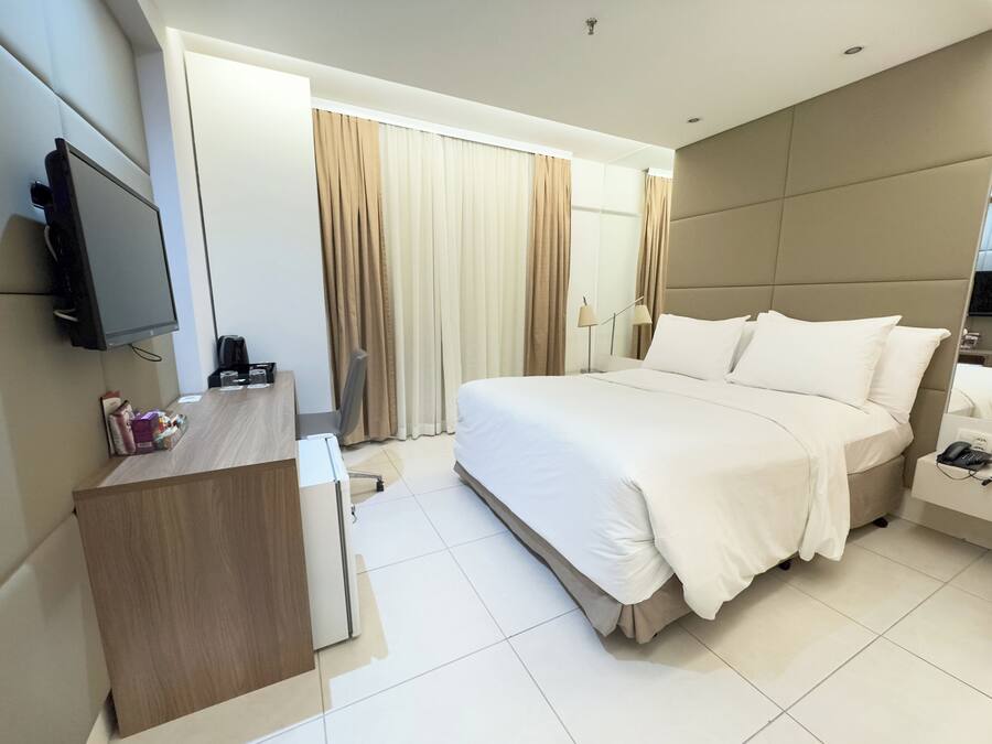 A modern hotel room with a large bed, a desk, a flat-screen TV, and a bedside table with a lamp.