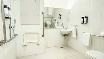 A modern bathroom with a shower, toilet, sink, and handrails.