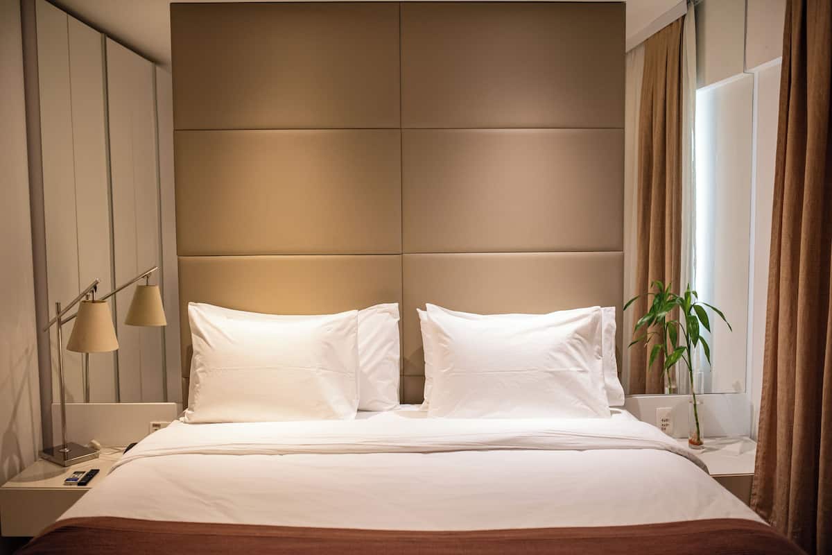 Een hotelkamer met een groot bed, een nachtkastje met een lamp, een bijzettafeltje met een telefoon en een raam met gordijnen.