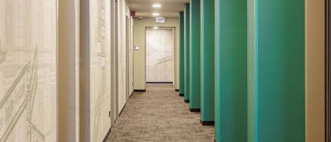 A hallway with carpeted floors, green lockers, and a door at the end.