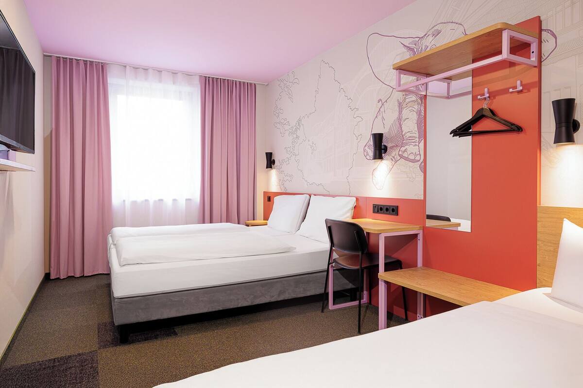 Ein Hotelzimmer mit Bett, Schreibtisch, Stuhl, Spiegel und einer Karte an der Wand.