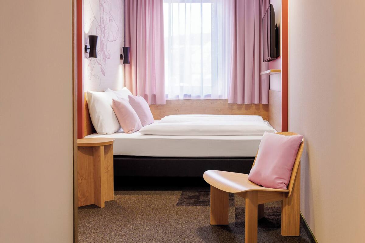 Ein Schlafzimmer mit einem Bett, einem Sessel, einem Fernseher und einer Wandlampe.