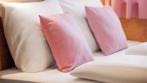 A bed with white and pink pillows, a wooden headboard, and a window with blinds. - McDreams Hotel Wuppertal City (Wuppertal)