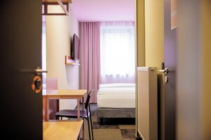 Habitación de hotel con cama, escritorio, silla, televisor y radiador.