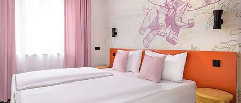 A hotel room with two beds, a large window with pink curtains, and a wall mural of an elephant.