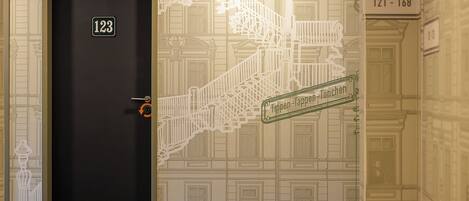 A hotel room with a dark door marked with the number 123, a staircase with a white railing, and a wall with a detailed architectural pattern.