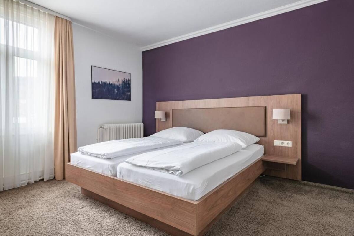 A double bed with a wooden headboard, a bedside table with a lamp, and a framed picture on the wall.