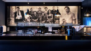 Een bar met een groot poster waarop een groep mensen, glazen en flessen staan afgebeeld.