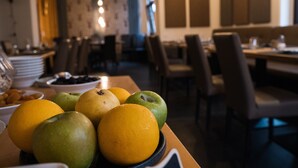 Een eetgedeelte met tafels en stoelen, een schaal fruit op de tafel en uitzicht op het interieur van het restaurant.