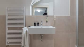 Une salle de bain avec un lavabo blanc, un porte-serviettes avec des serviettes, un miroir et un espace douche.