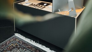 Een kamer met een bureau, een Apple iMac, een kamerbreed tapijt met een patroon en een plank met potten.