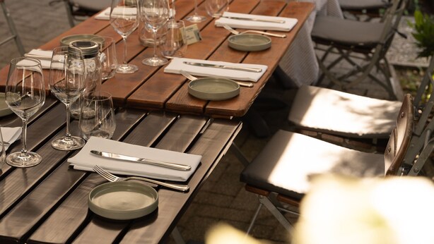 Een terras met tafels voor twee personen, met houten tafels en metalen stoelen.