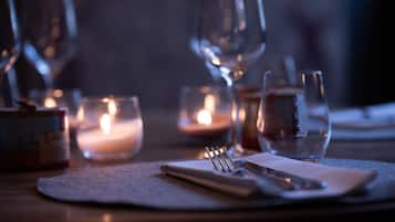 Una mesa tenuemente iluminada con velas, copas de vino y cubiertos, evocando un ambiente romántico para cenar.