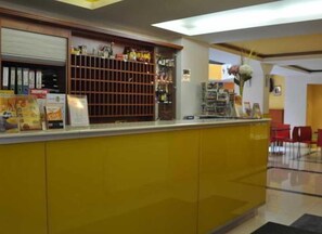 Zona de recepción con mostrador, tablón de anuncios y una exhibición de revistas.