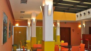 A hotel lobby with orange chairs and tables, a black and white striped floor, and a ceiling with exposed beams. - City Central (Prague)