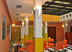 Un espacio interior muy luminoso con paredes naranja y amarillas, varias zonas de estar con sillas color naranja, y un techo con tragaluces.
