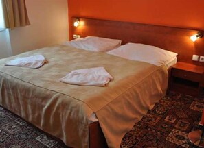 Una habitación de hotel con una cama, dos almohadas, una mesita de noche y una alfombra estampada.