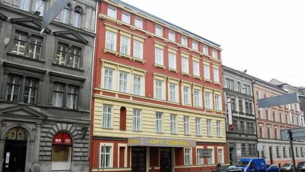 A multi-story building with a red and yellow facade, a sign indicating a city center, and several parked cars. - City Central (Prague)
