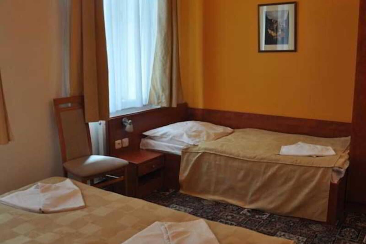 A hotel room with a bed, a bedside table, a chair, and a window with curtains.