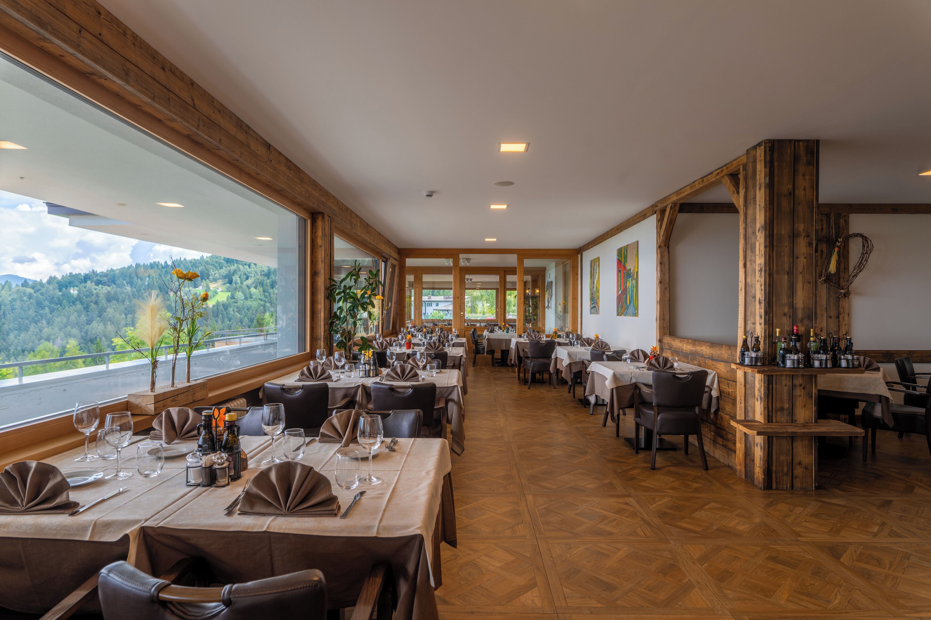 Ein Restaurant mit mehreren Essplätzen, großen Fenstern mit Blick ins Freie und Holzbalken an der Decke.