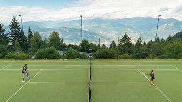 Cancha de tenis con dos jugadores, rodeada de montañas y árboles.