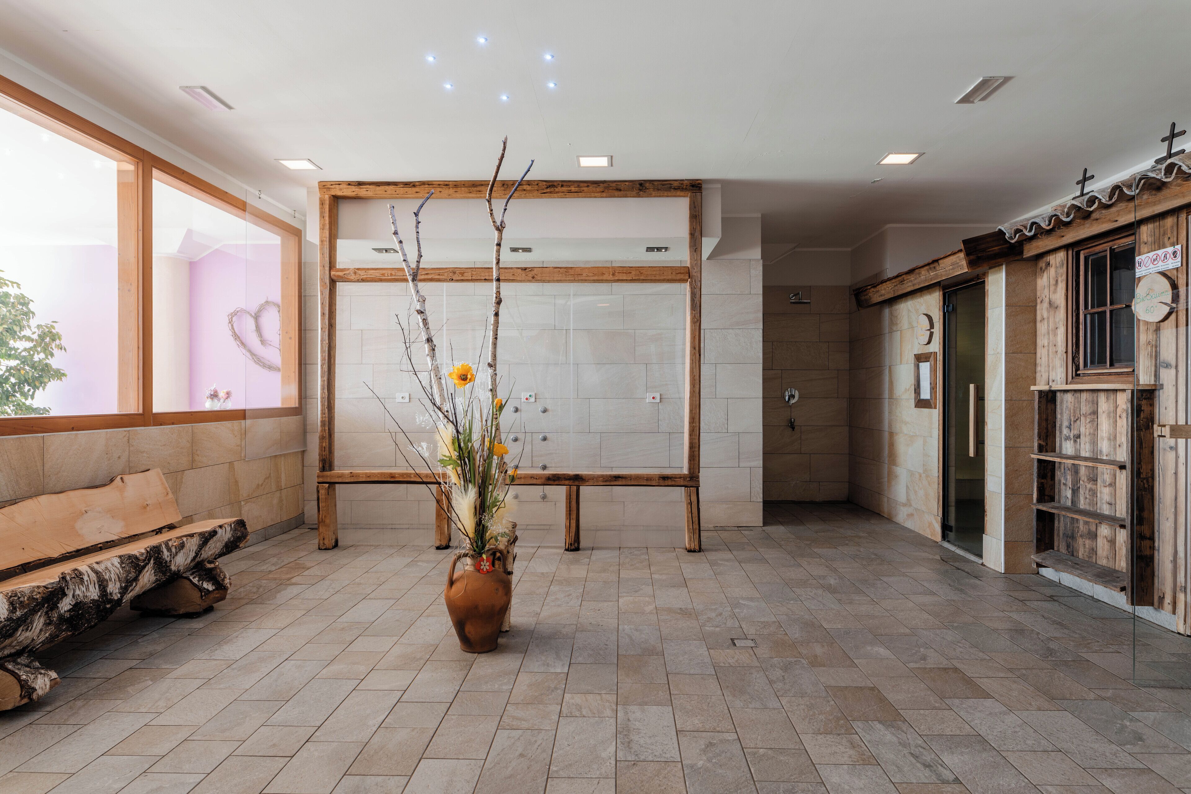 A spacious lobby with a wooden bench, a large vase with flowers, and a tiled floor.