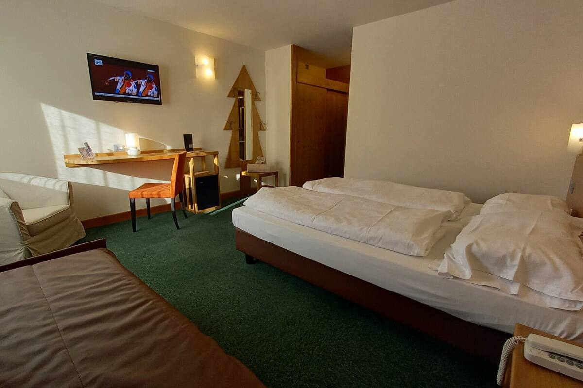 A hotel room with a bed, a desk, a chair, a TV, and a small table.