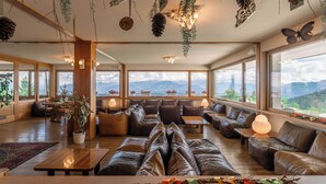 Un amplio salón con sofás de cuero, mesas de madera y grandes ventanales con vistas a la montaña.