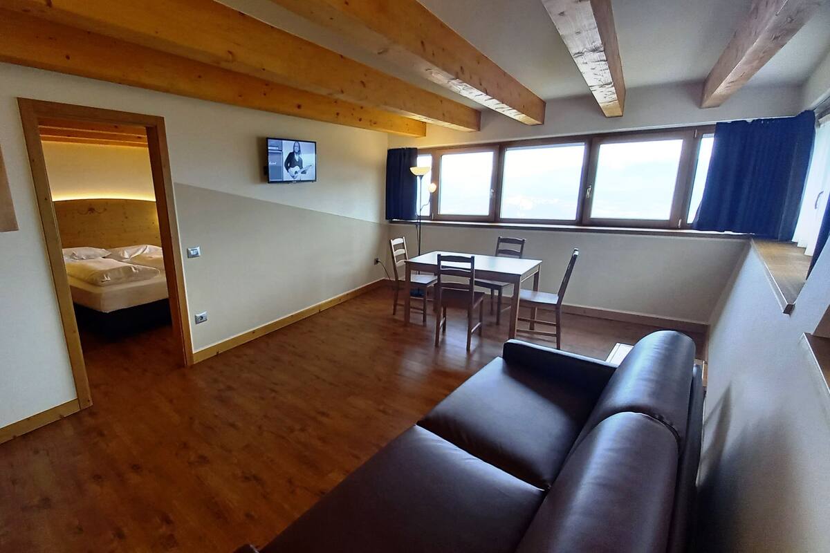 A cozy room with a wooden floor, a bed, a TV, a dining table with chairs, and a couch.