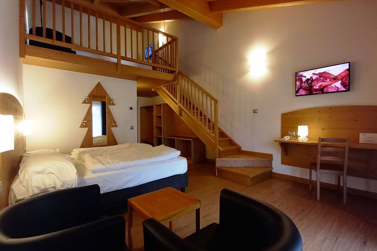 A bedroom with a bed, a desk, a chair, a TV, and a staircase.