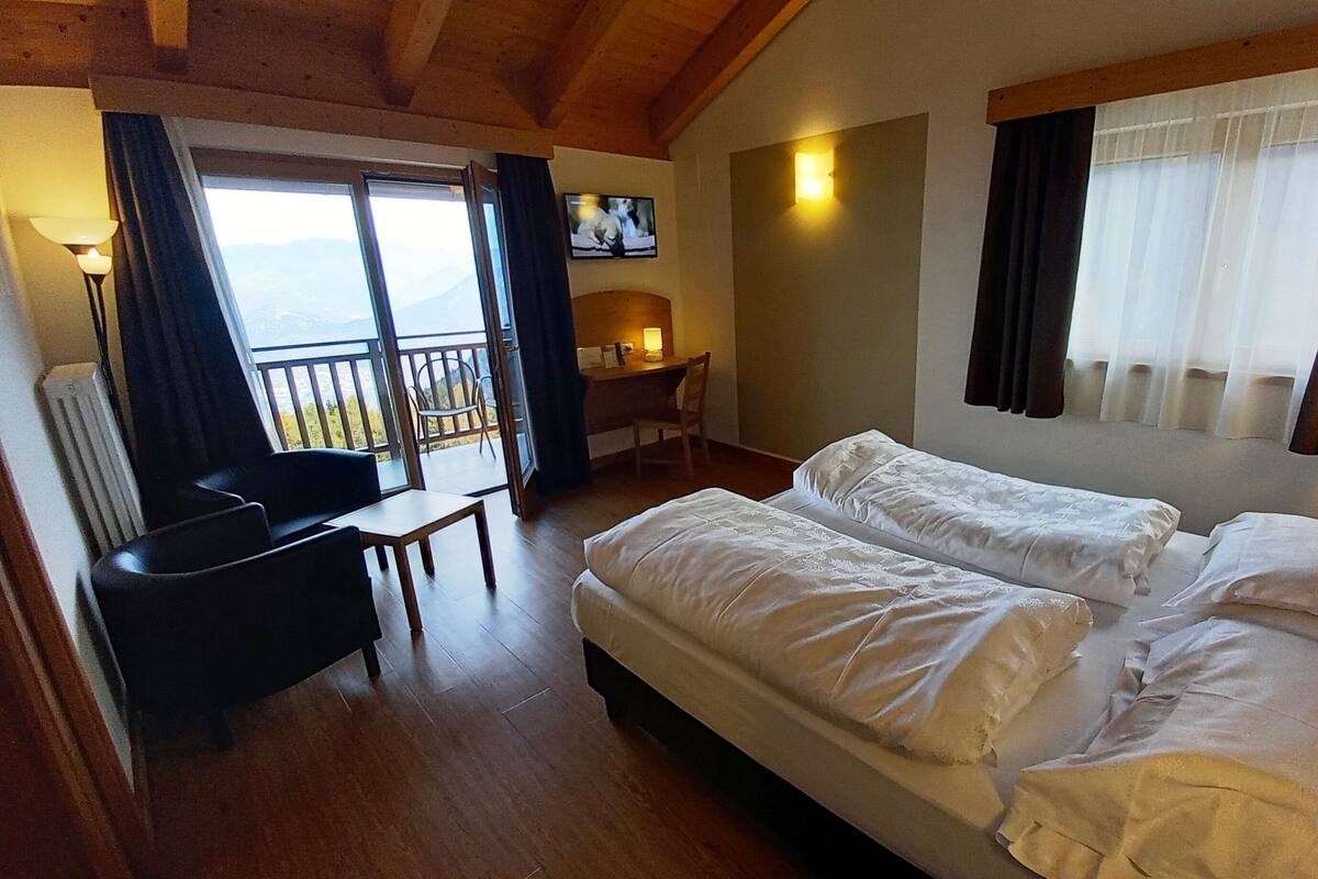 A hotel room with two beds, a desk, a chair, and a view of the outdoors.