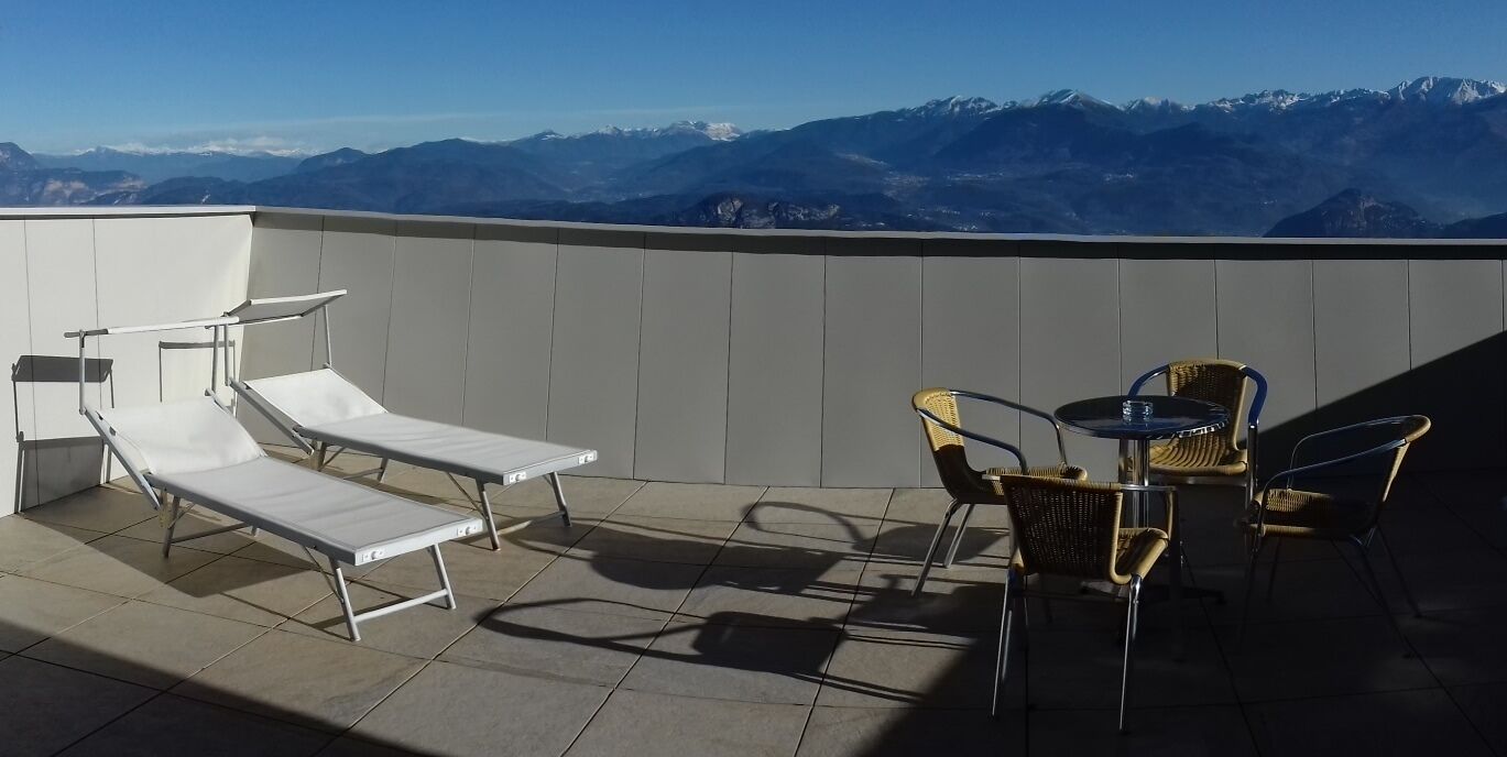 Een terras op het dak met loungestoelen en een tafel, met uitzicht op een bergketen.
