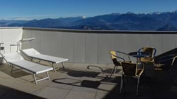 Terraza en la azotea con sillones de descanso y una mesa, con vistas a una cordillera.