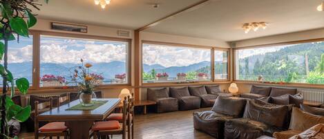A spacious room with a wooden dining table, brown leather sofa, and large windows offering mountain views.