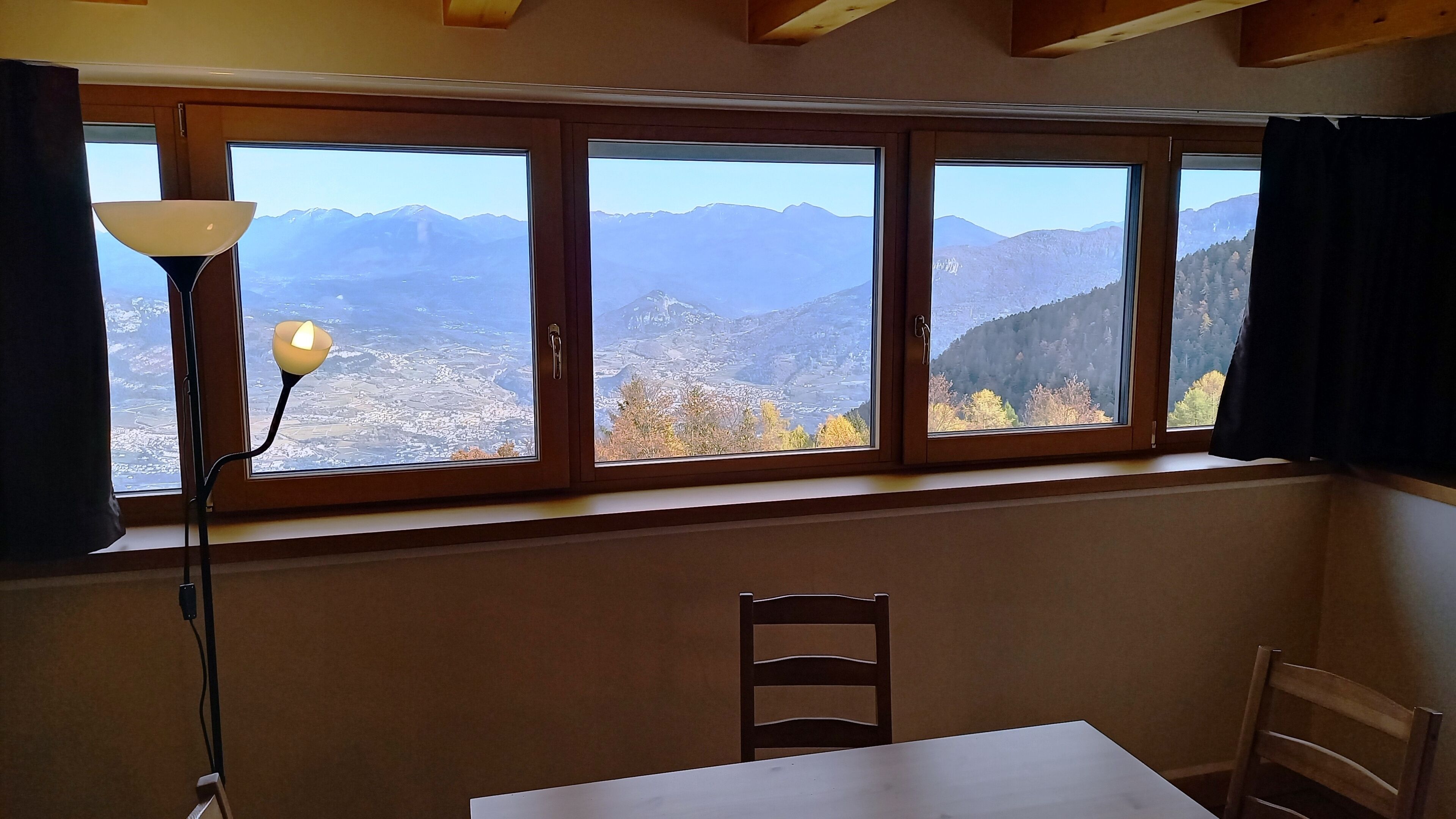 A room with a table and chairs, a window with a view of mountains, and a lamp.